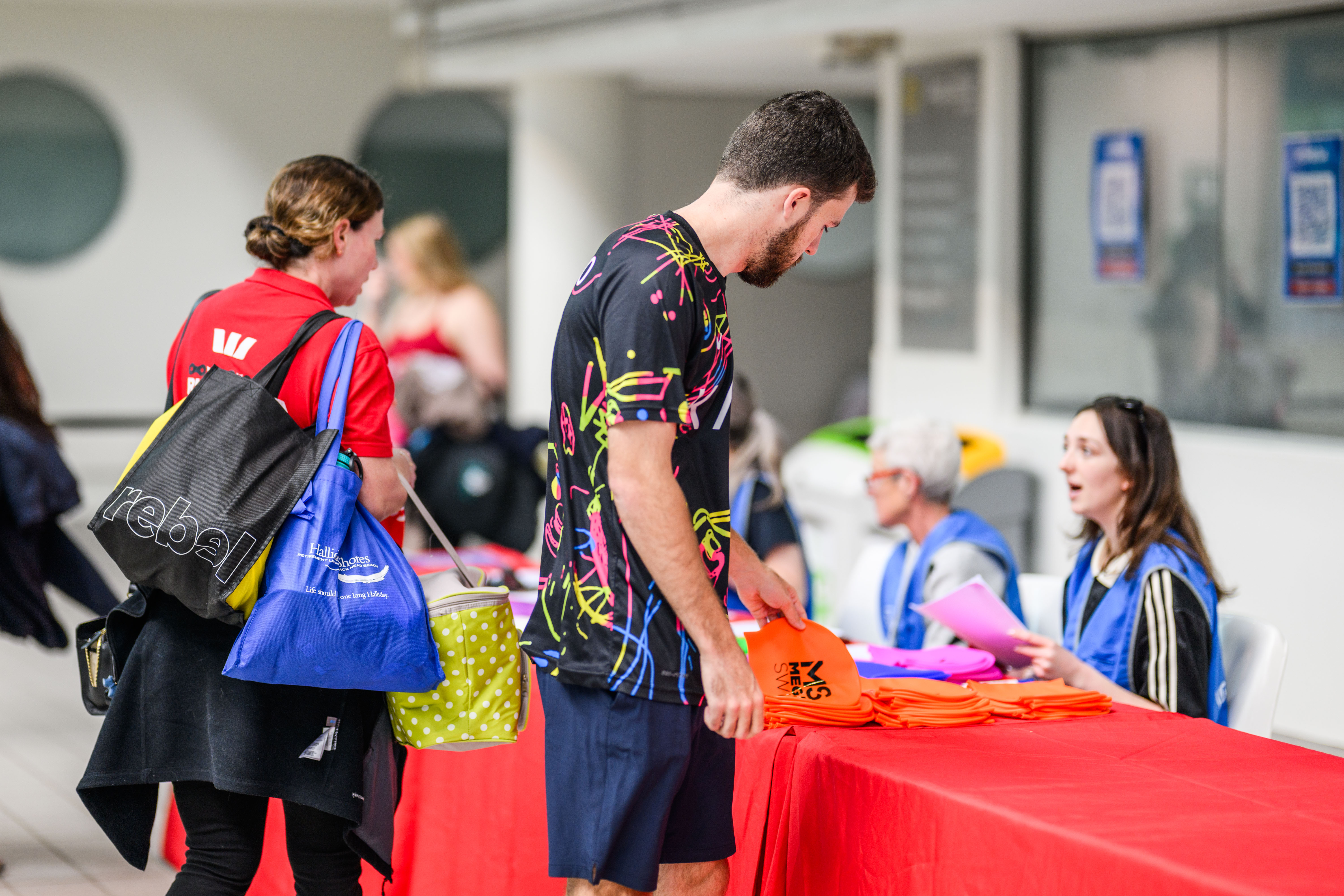 a table with red cloth with a participant coming up to the desk to grab a bib